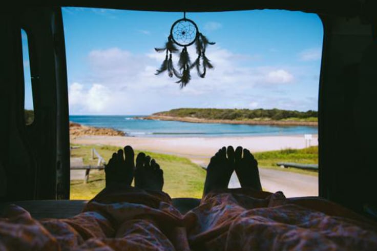 2 people waking up to a beach view in a campervan