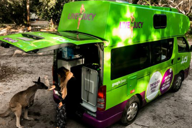 Girl sitting in the back of a JUCY campervan with a kangaroo ouside