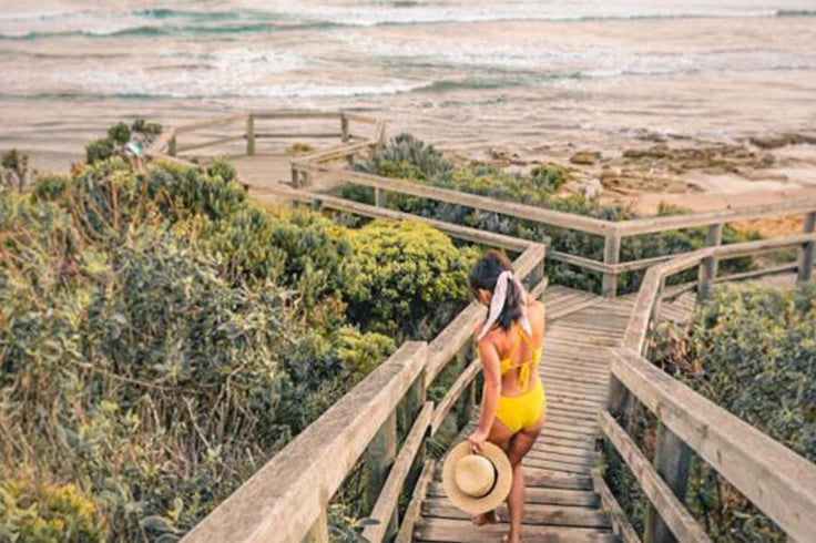 girl in swimsuit walks down steps at beach in australia