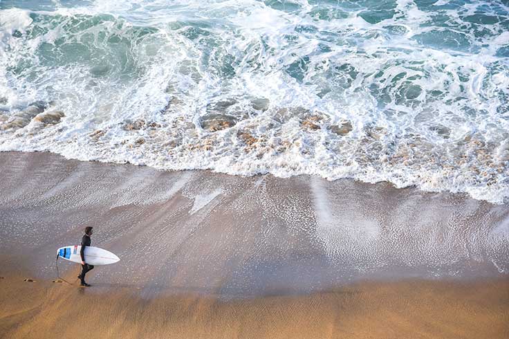 A guy walking along the Bells Beach shores whilst holding his surf board