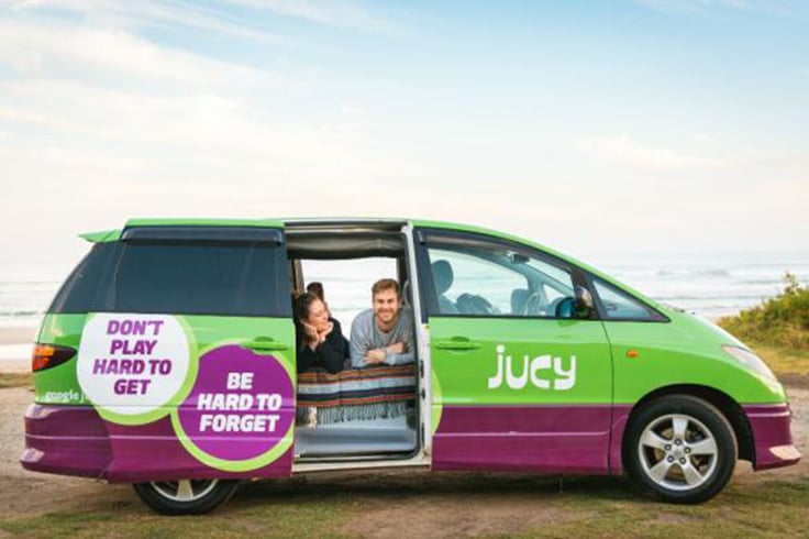 two people in a bed in the back of a jucy campervan