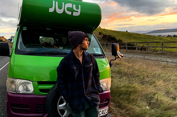 Boy stands in front of JUCY Camper overlooking Taupo sunset
