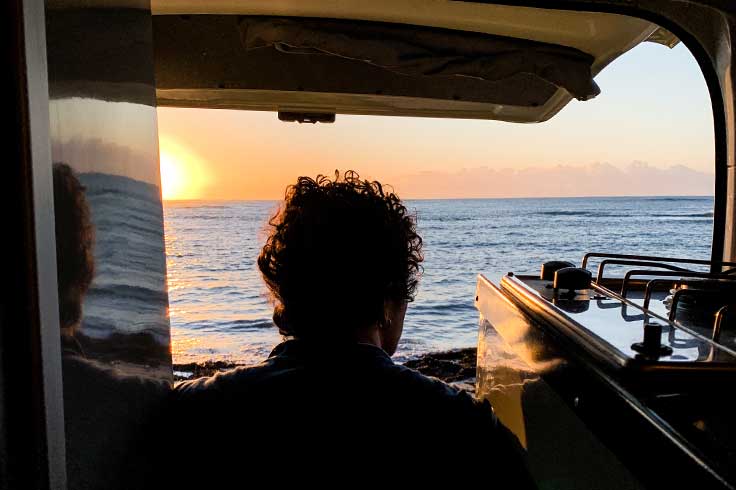 Man looking out of back of campervan at sunset