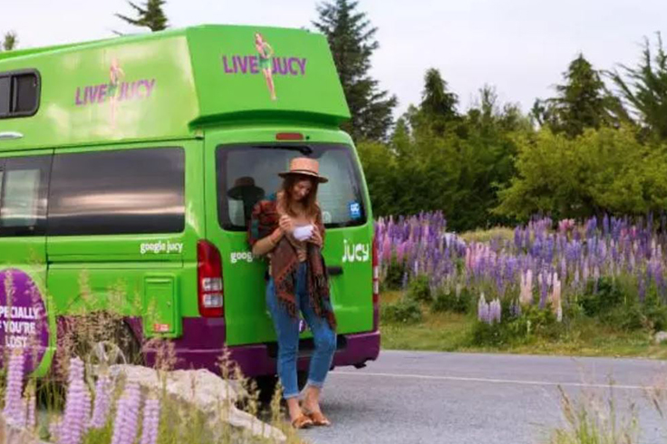 Woman posing at the back of a campervan with purple flowers