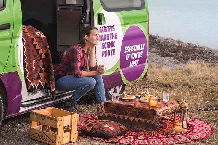 Girl having a coffee sitting in opening of JUCY camper door