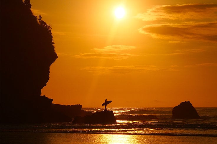 Surfer standing on rock on West Coast beach