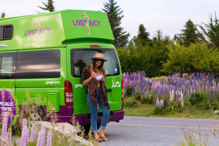 Woman standing outside campervan near field of purple flowers
