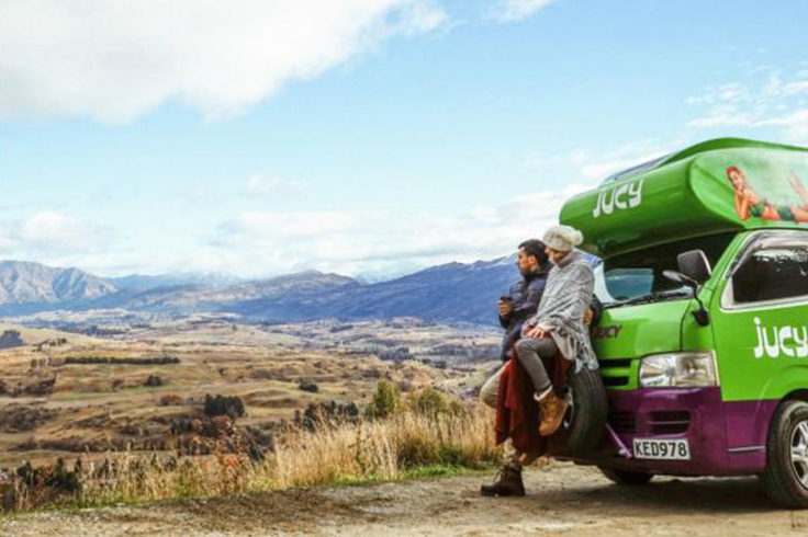 Couple leaning on a JUCY campervan