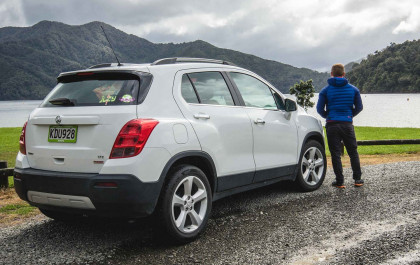 man looks on lakefront with parked suv
