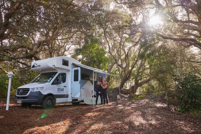 Couple in wetsuits outside Star RV motorhome with awning